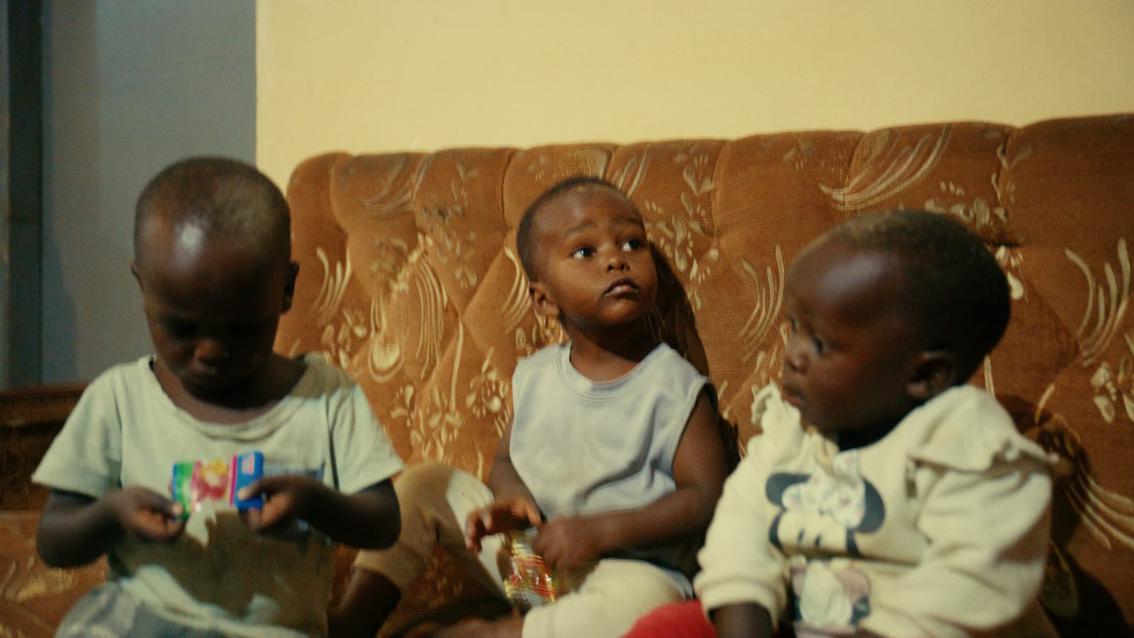 Drei kleine Kinder sitzen nebeneinander auf einem Sofa und spielen.